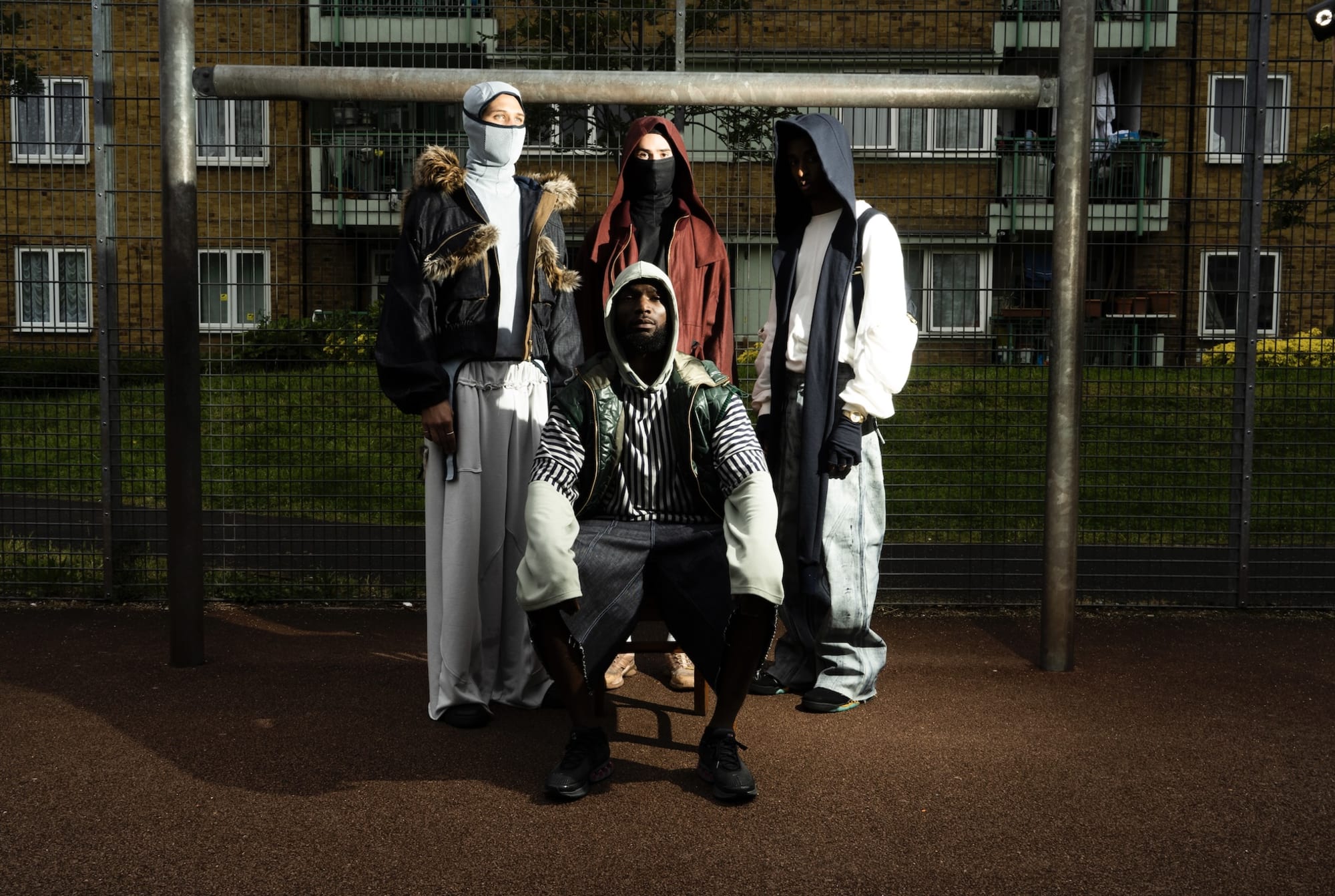 Four males on an estate standing in front of a wire fence on sportswear and masks.