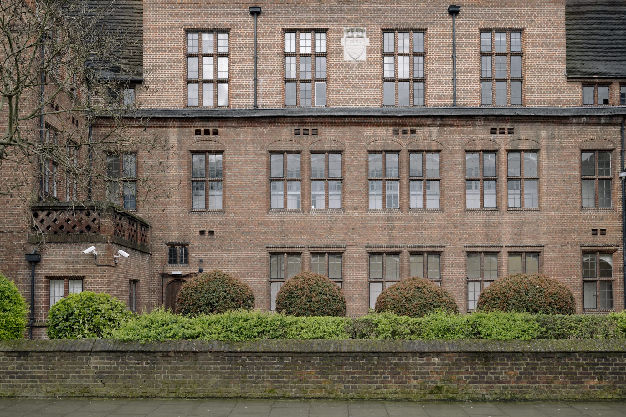 An old brick building with ornate windows and neatly trimmed hedges in front