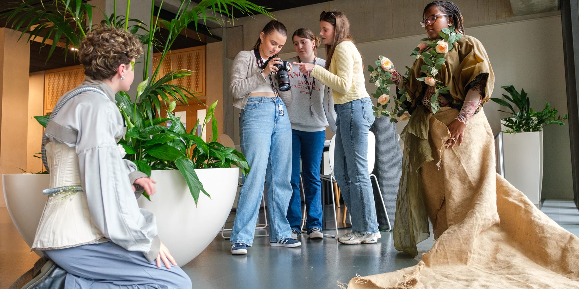 A group of students working together on a photoshoot. The models are styled in neutral floral/ romantic garments. There are plants in shot.