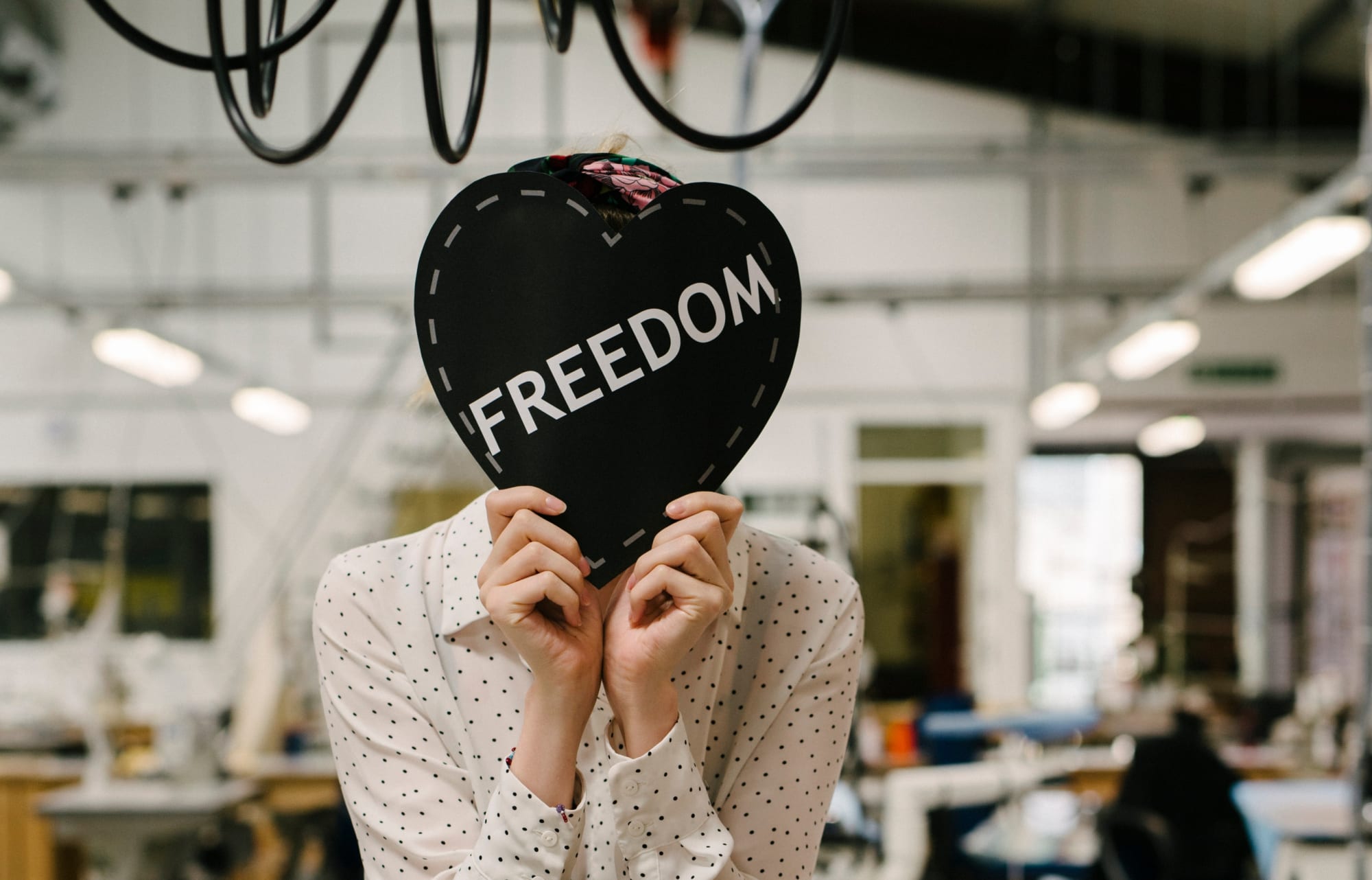 Woman holding a black heart over her face with the word, 'Freedom' written on it.