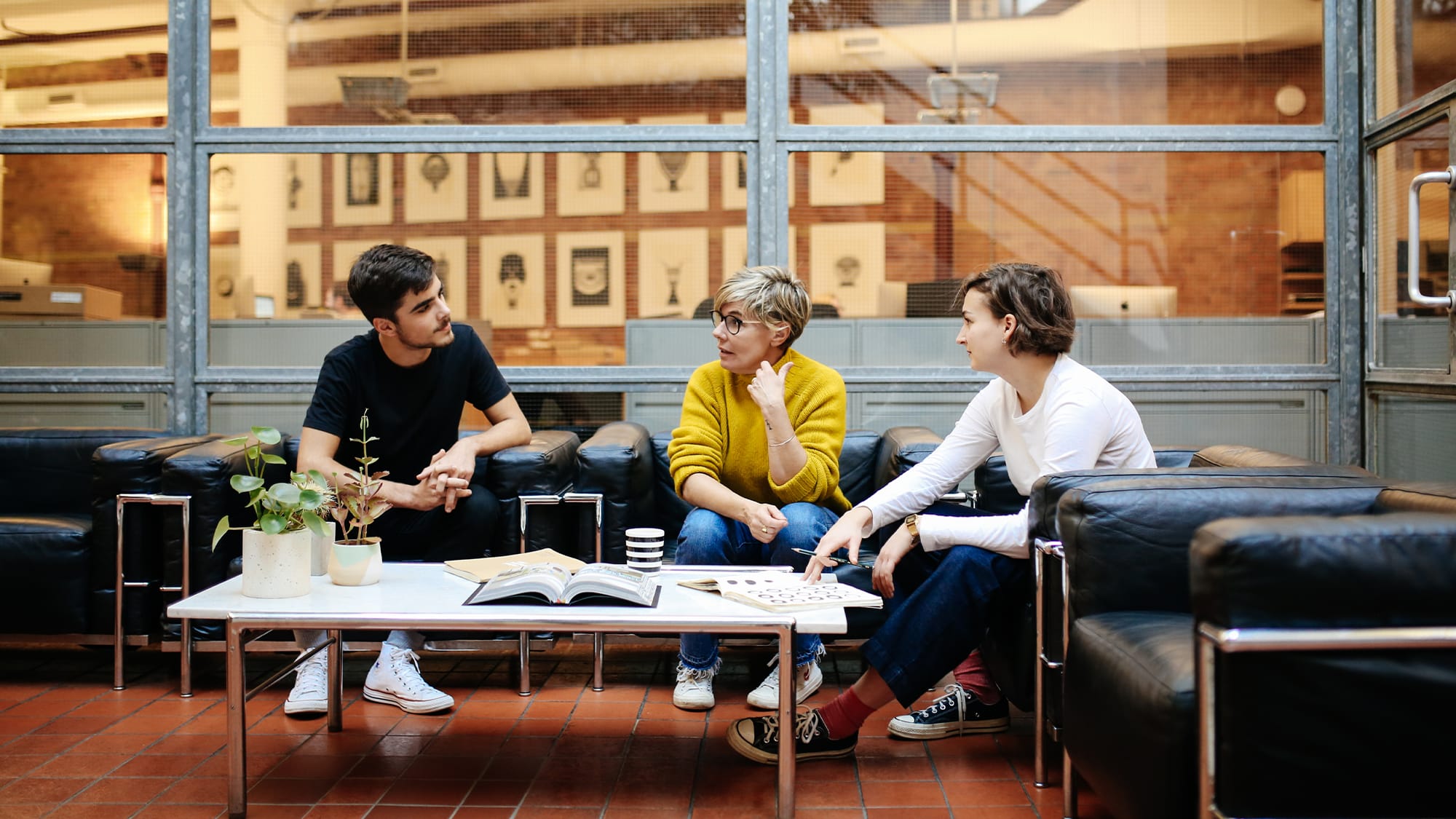 Two students sit at a table with a mentor looking through sketchbooks