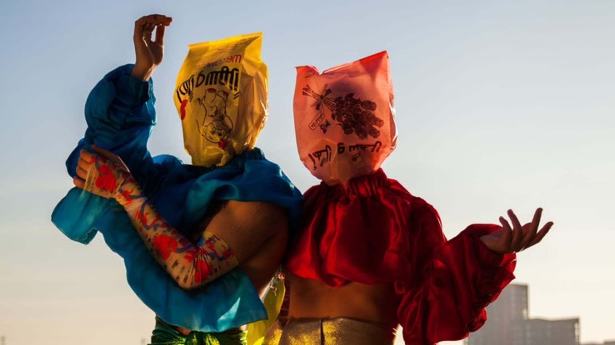 Models on the beach in bright coloured clothing and bags covering their faces.