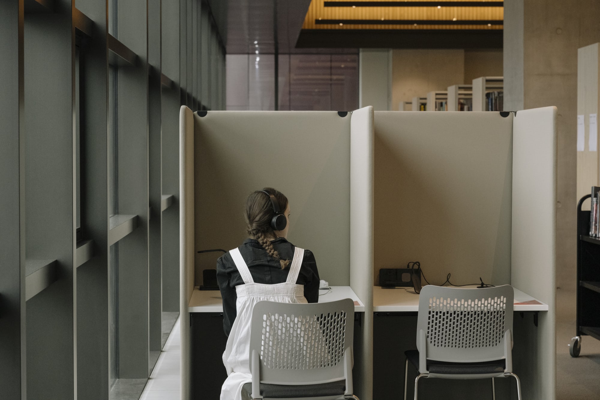Person with back facing the camera with headphones on, at an enclosed desk.