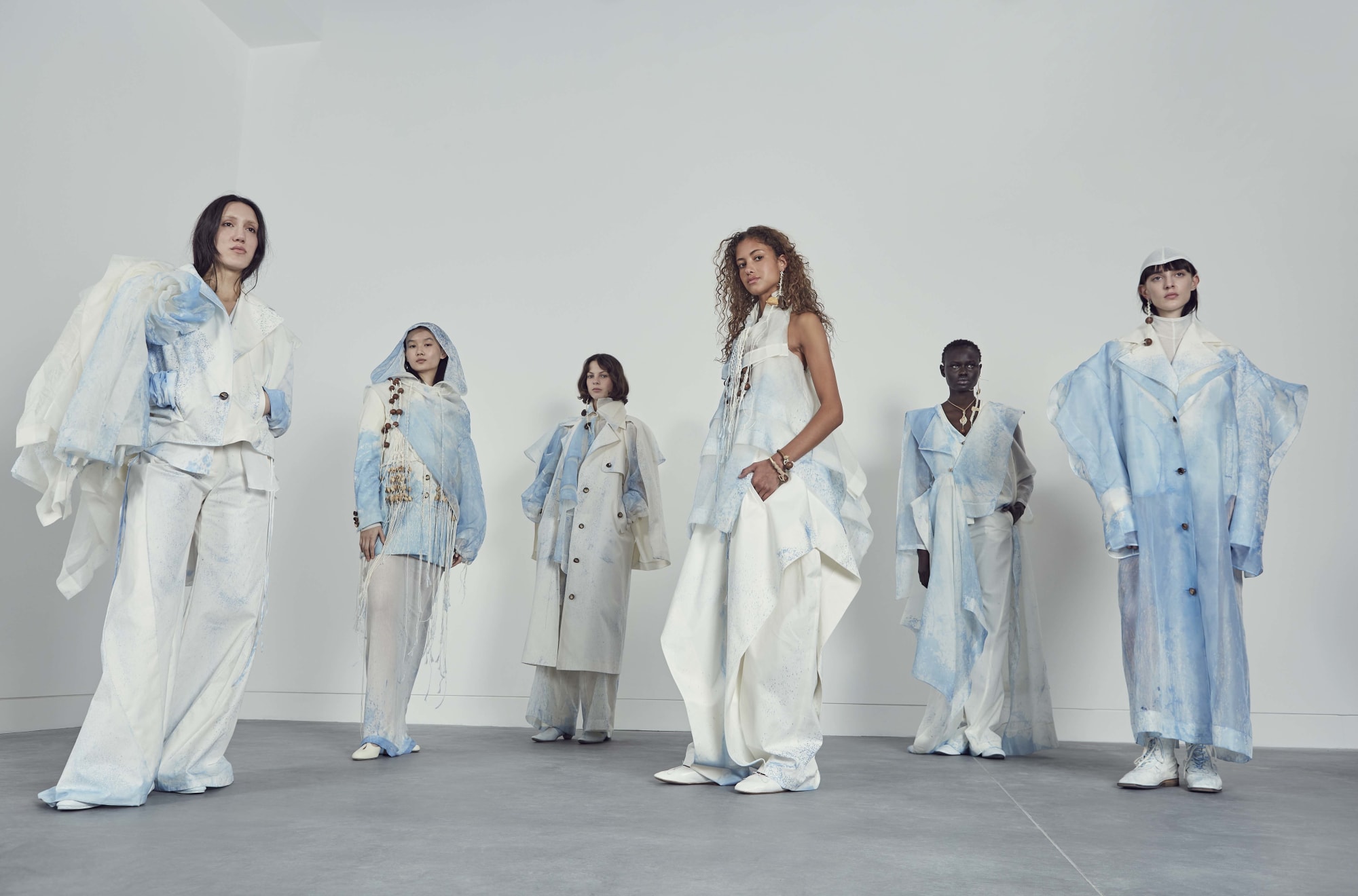 6 models in pale blue and white outfits, standing backstage.