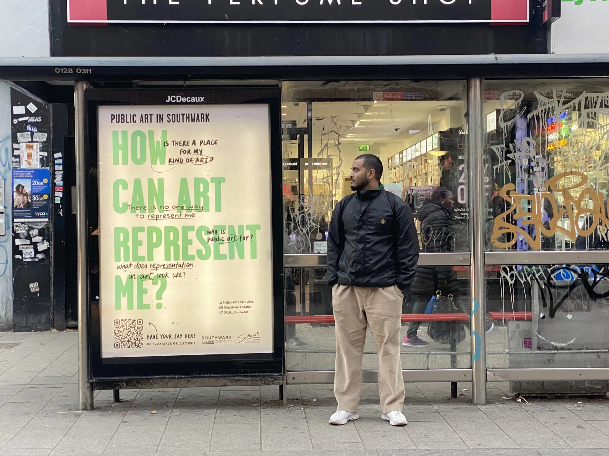 Man standing at bus stop, next to a piece of public art in the bus-stop shelter.