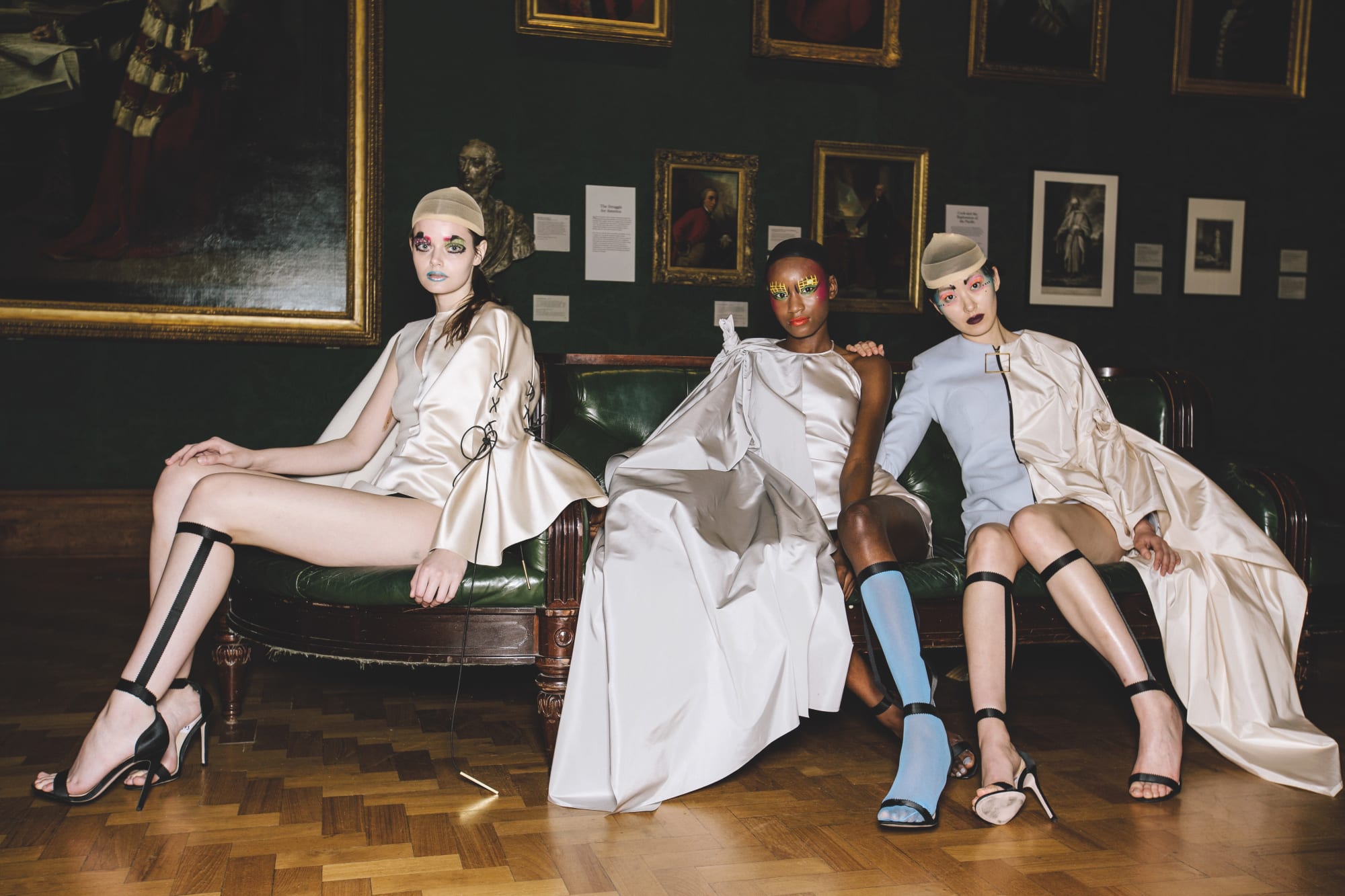 Female models dressed in glossy off white garments, sitting on a sofa at the National Portrait Gallery - by fashion designer Emma Bergamin Davys 