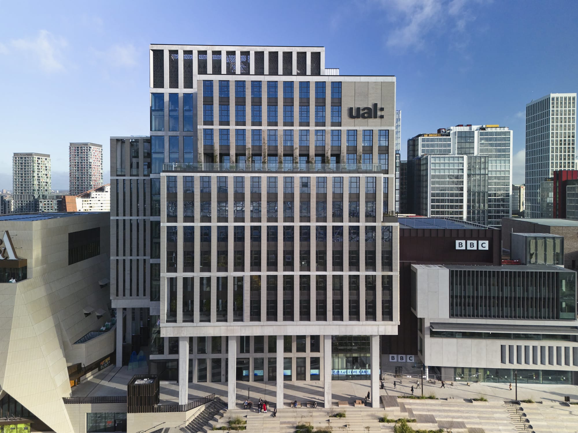 Exterior view of the LCF East Bank Building - a tall block shaped building with many windows, next to a lower building with a BBC sign, shot against a blue sky.