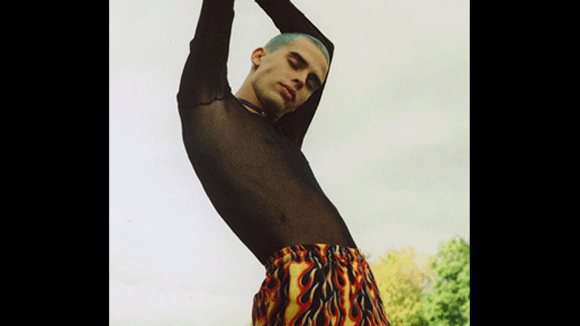 Male model with blue hair and black mesh top with his arms over his head