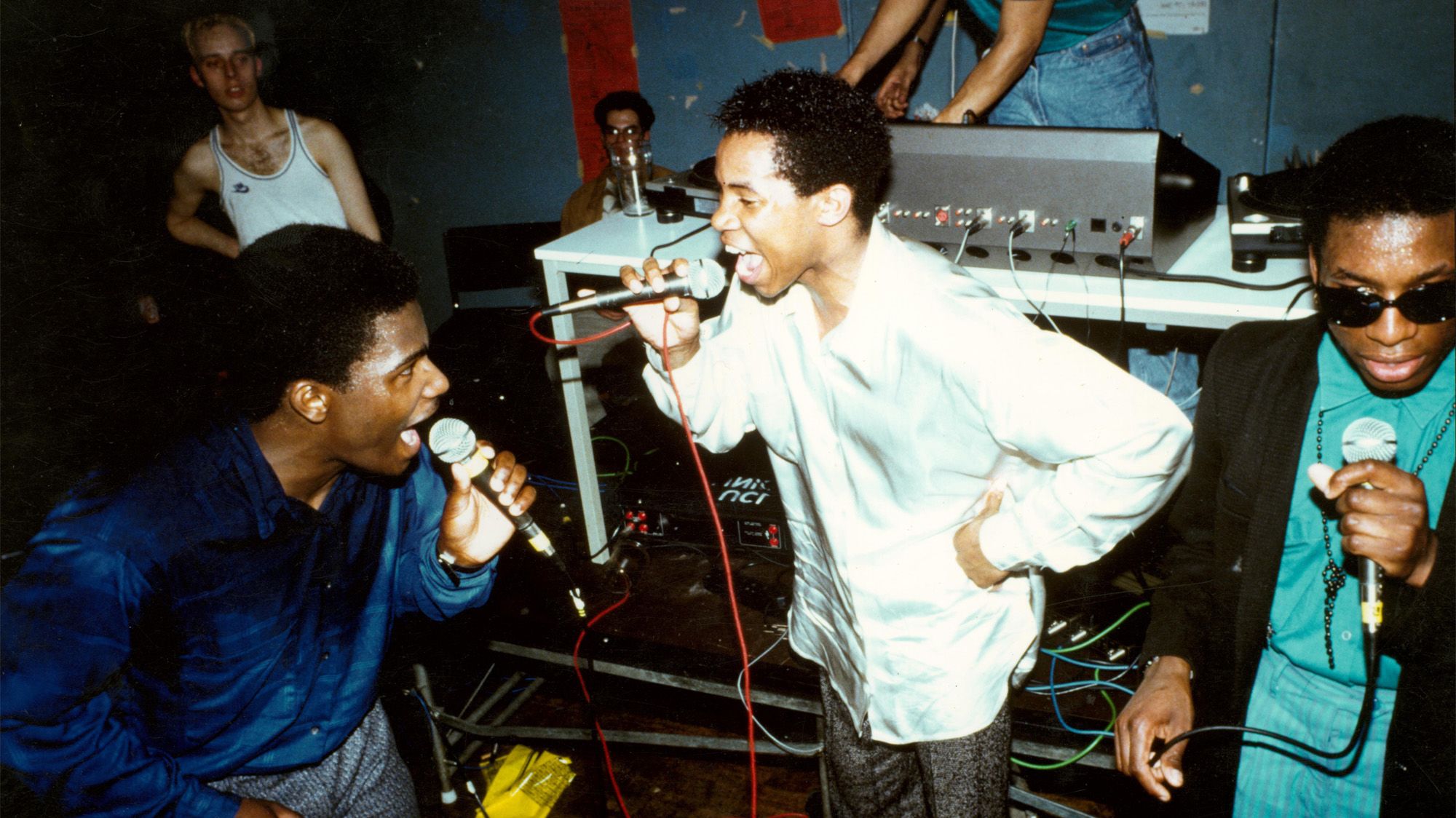 Three people standing together as a group singing into microphones in a club setting