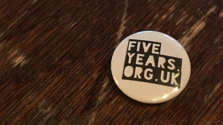 A badge which says 'fiveyearsgallery.org.uk' on top of a wooden table