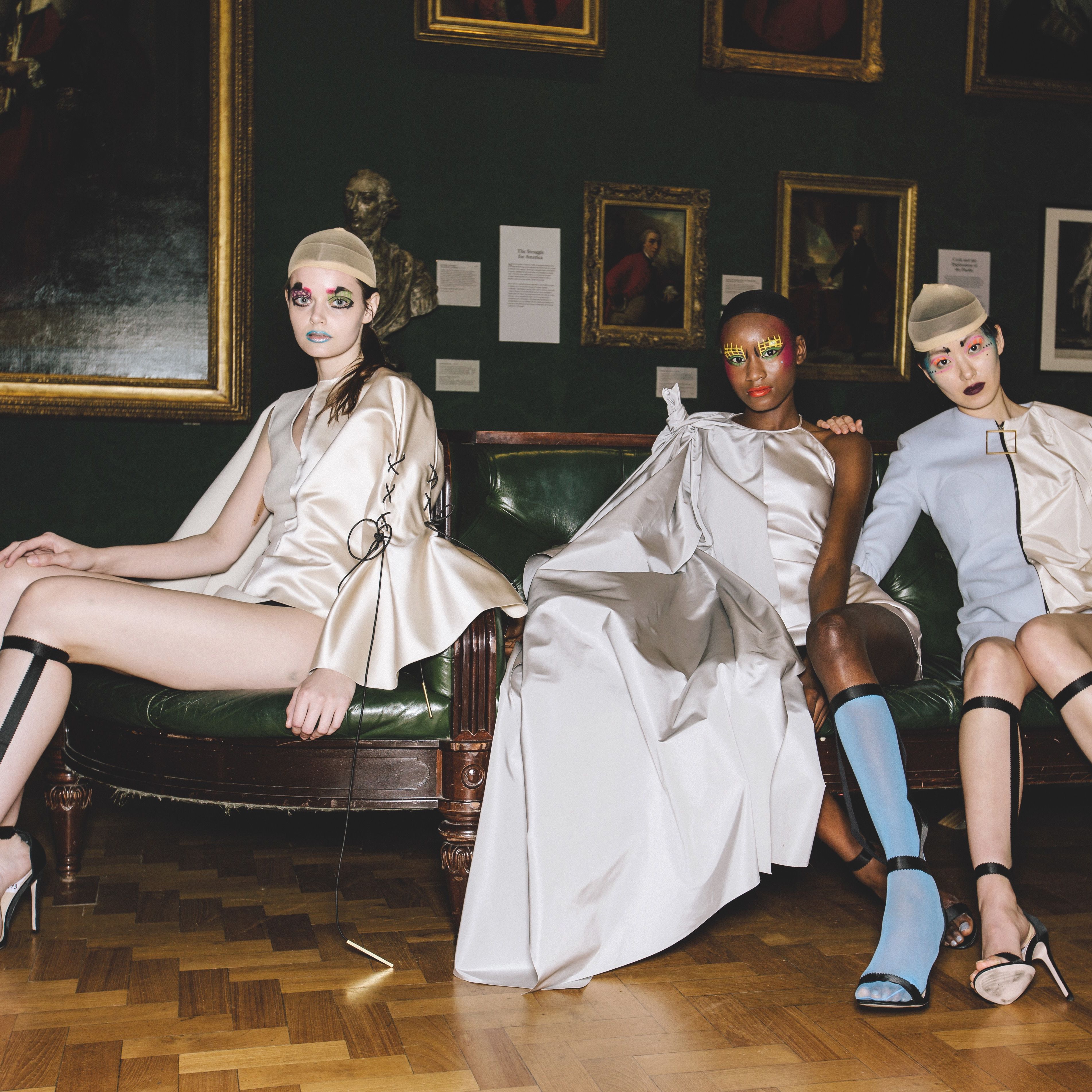 Female models dressed in glossy off white garments, sitting on a sofa at the National Portrait Gallery - by fashion designer Emma Bergamin Davys 