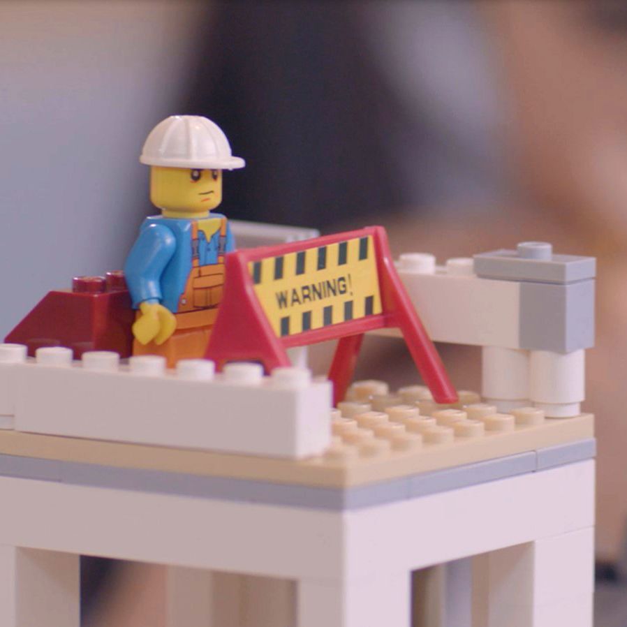 Close up still from a film. Lego tower with a lego construction worker.