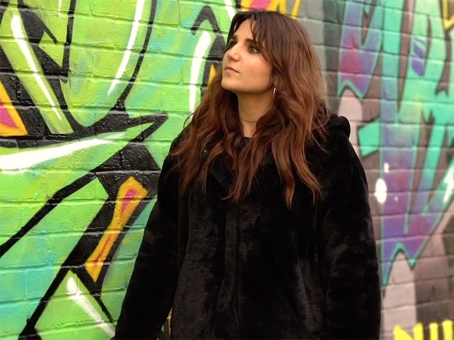 Revital stands in front of a heavily graffiti-ed brick wall.