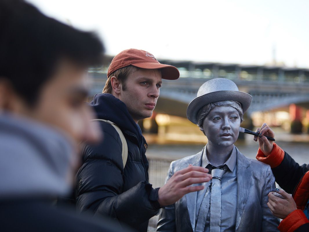 A make-up artist paints the face of an actor playing a living statue.