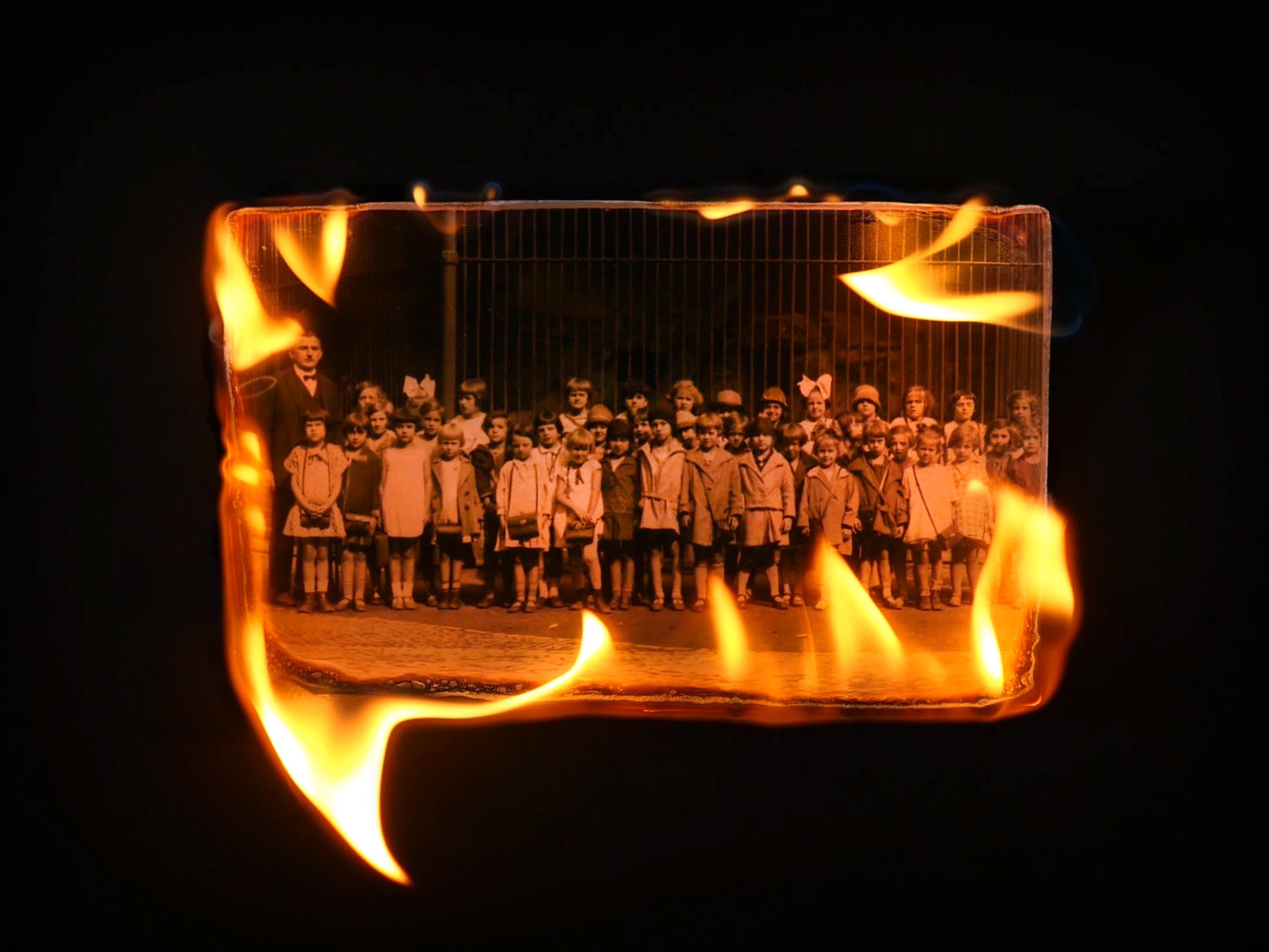 Video still of film For Leopold, featuring a photograph of children, its edges burning.