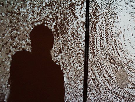 Image shows a white and grey light projection on the side of a building accompanied by a small shadow of someone standing in front of the light source.