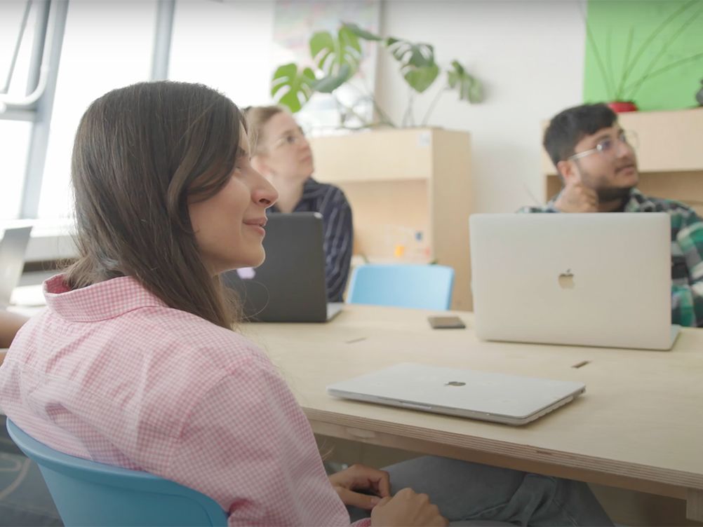People sit around a table and look off-screen at a presenter.