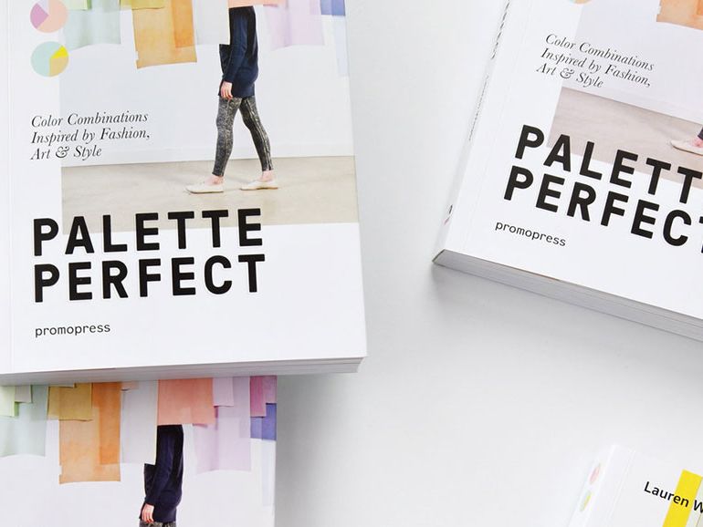 An arrangement of copies of Palette Perfect, the covers of which feature a single figure walking across a gallery space filled with hanging colour banners.