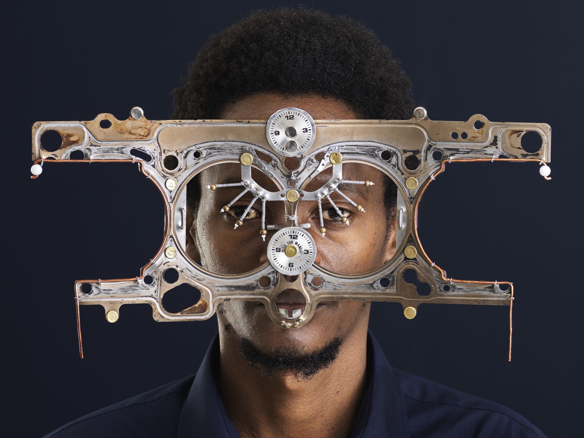 A portrait photo of a man of African descent looking into the camera, wearing oversized, futuristic glasses made out of metal