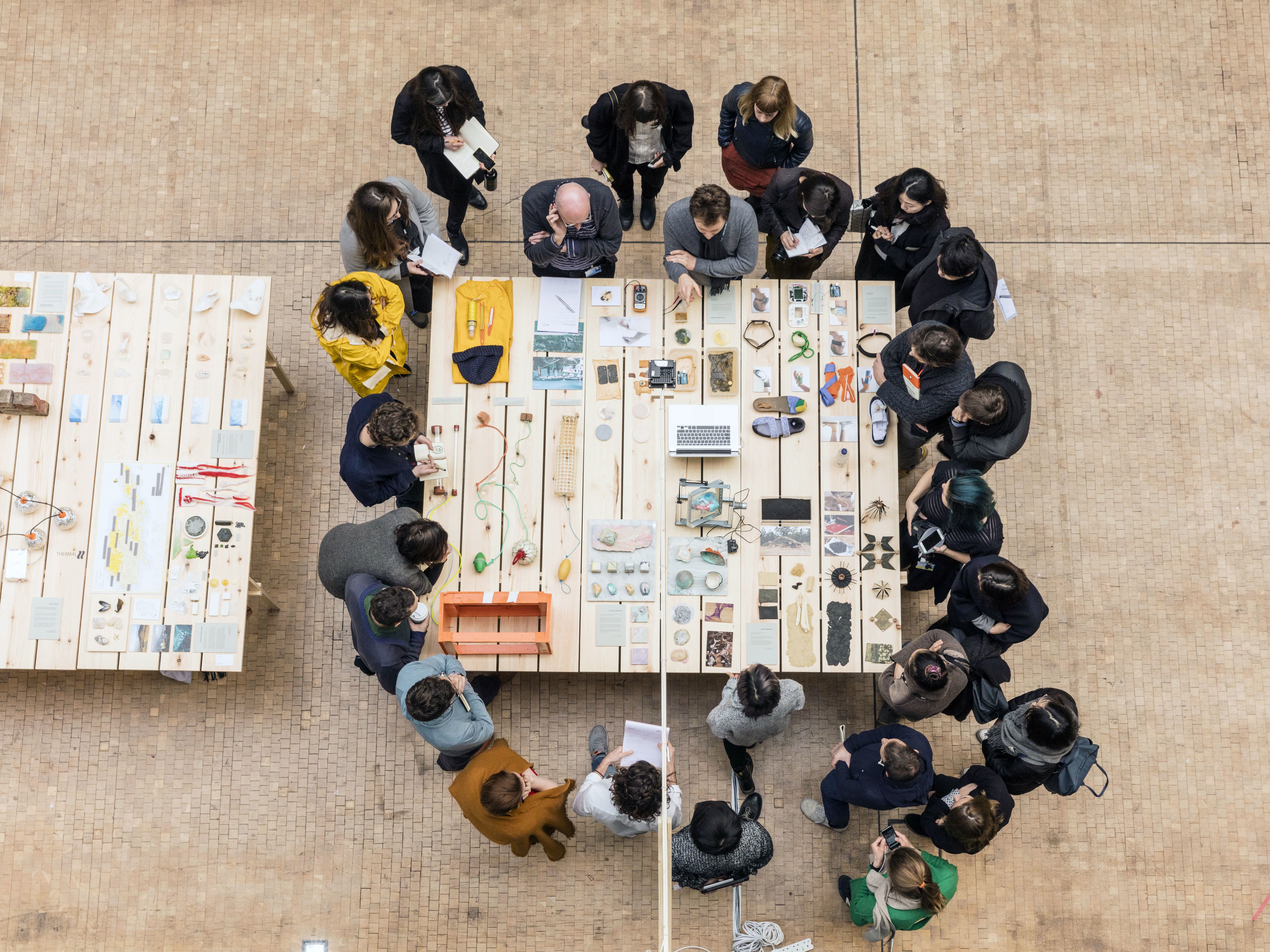 Group of people gathered around a table looking at different objects and devices