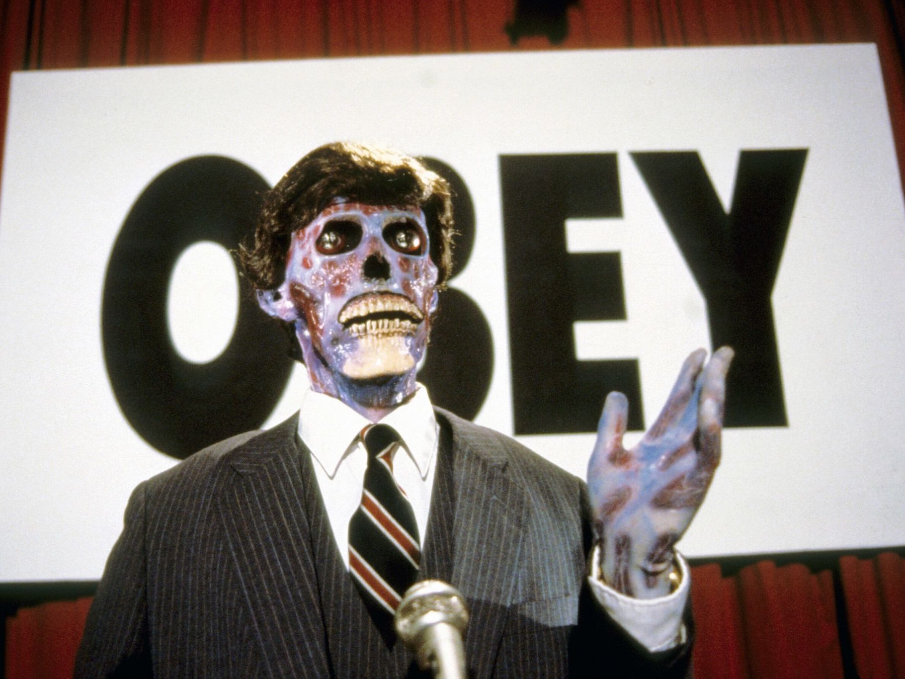 Skeleton in a suit next to sign that reads 'OBEY' 