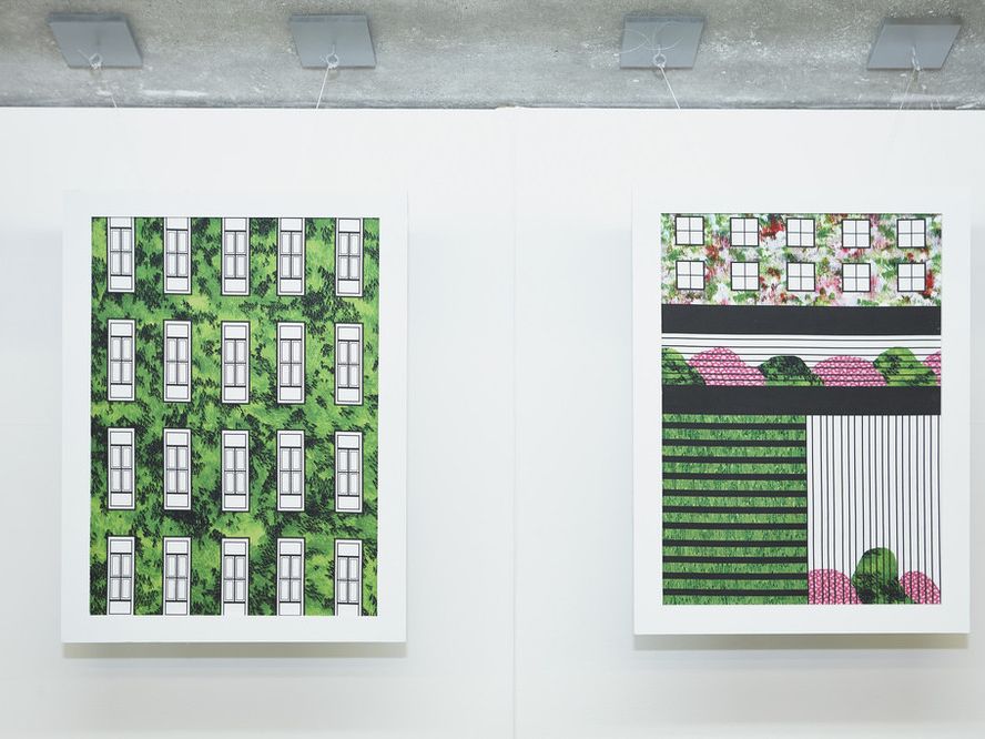 2 paintings in white frames on a white wall showing buildings and symmetrical designs integrated with the green of nature
