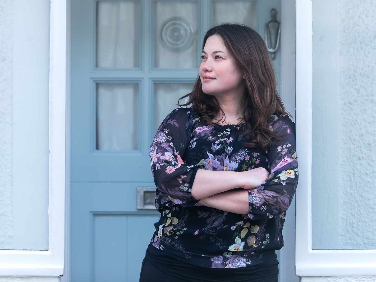 A woman stands in front of a door and looks away from the camera.