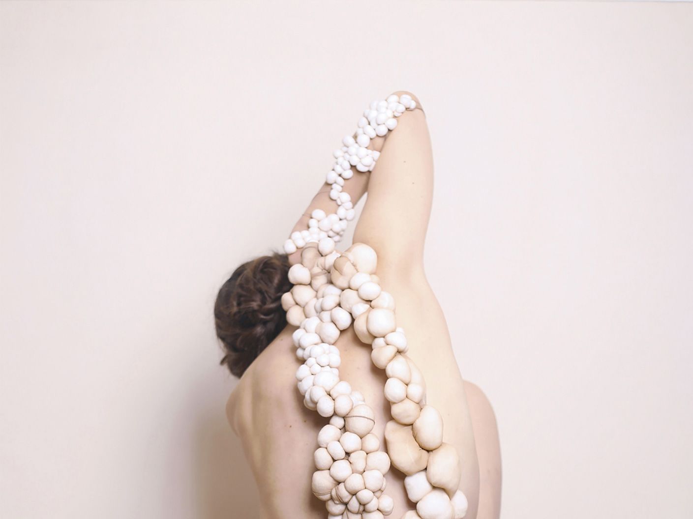 A naked figure is covered in round material objects.