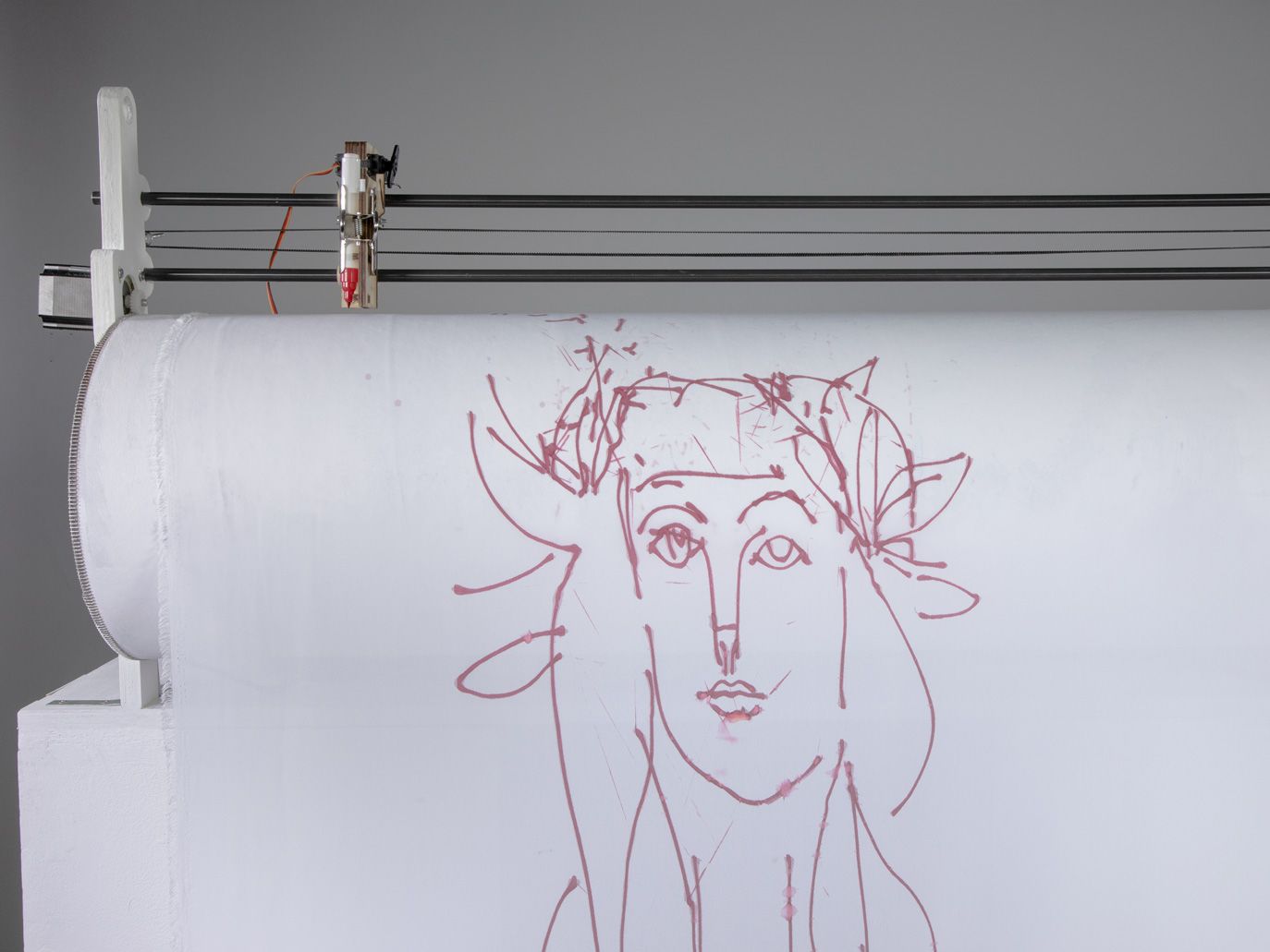 A robot holding sheet of fabric with a drawing of a Picasso-style face, with the sheet of paper on a roller with a pen held