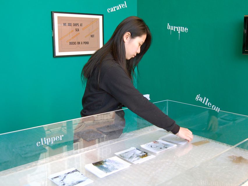 An Asian student setting up materials in an exhibition display against a forest green wall