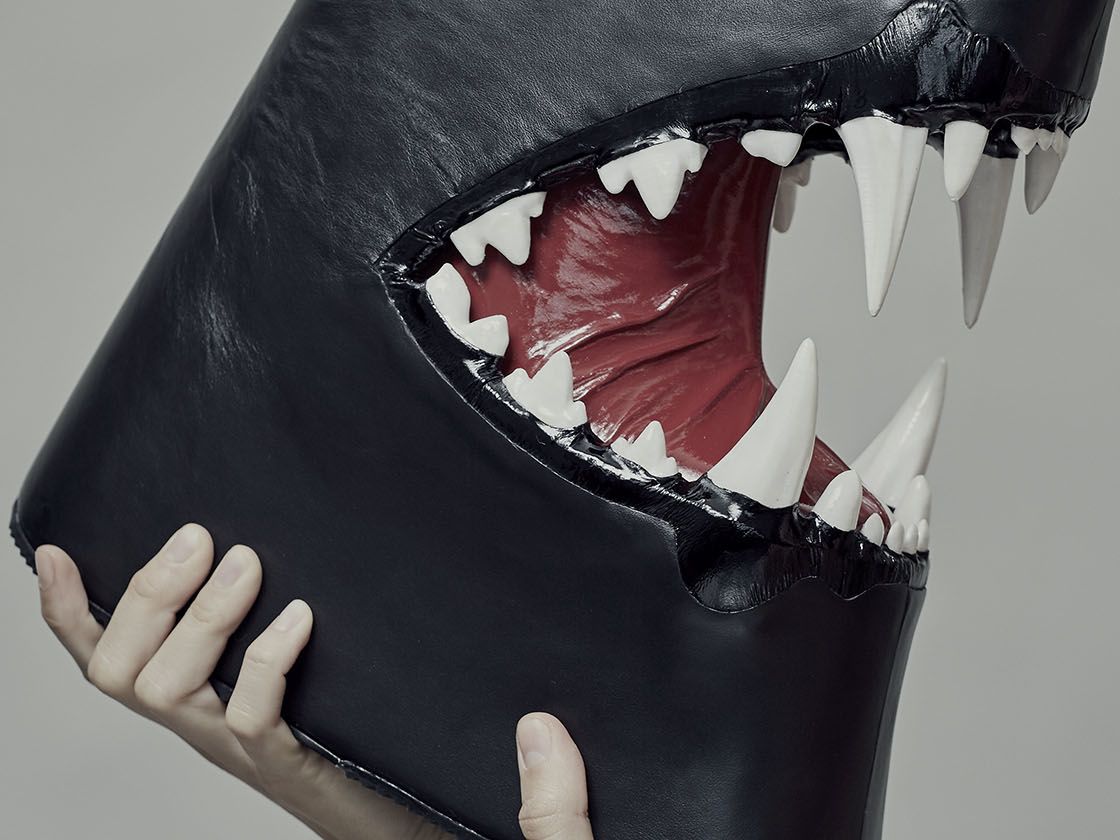 Black boot with sharp teeth held by female model screaming at it