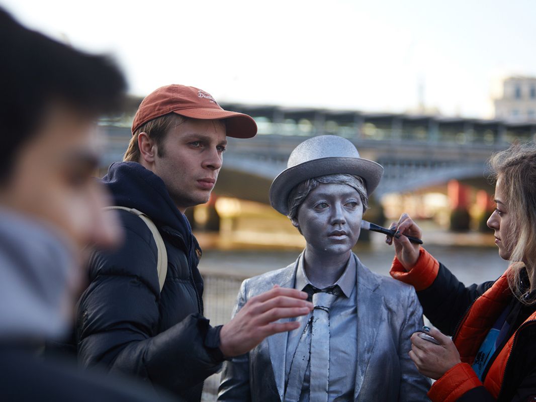 A make-up artist paints the face of an actor playing a living statue.