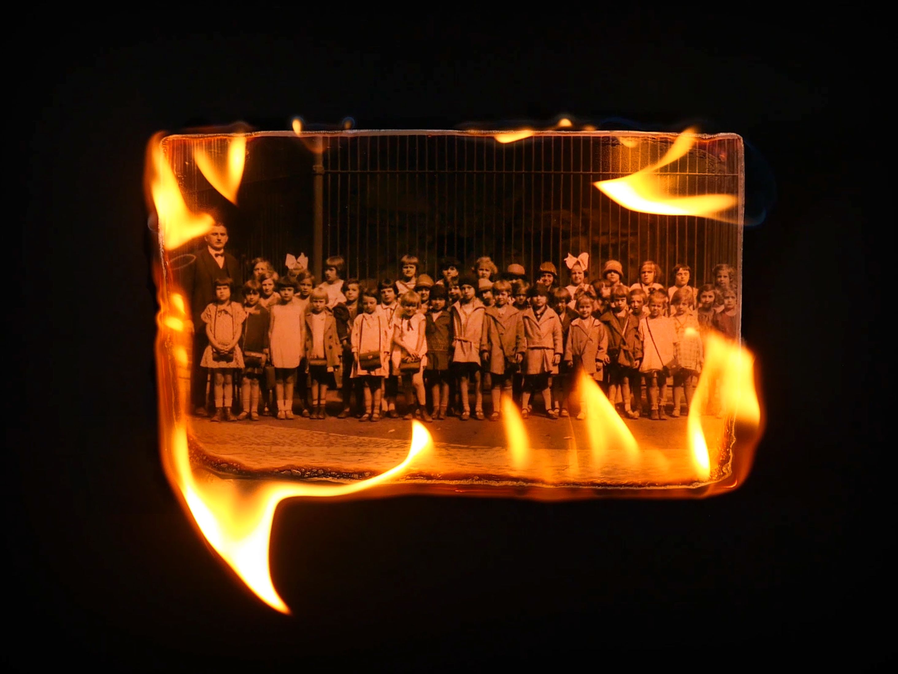 Video still of film For Leopold, featuring a photograph of children, its edges burning.
