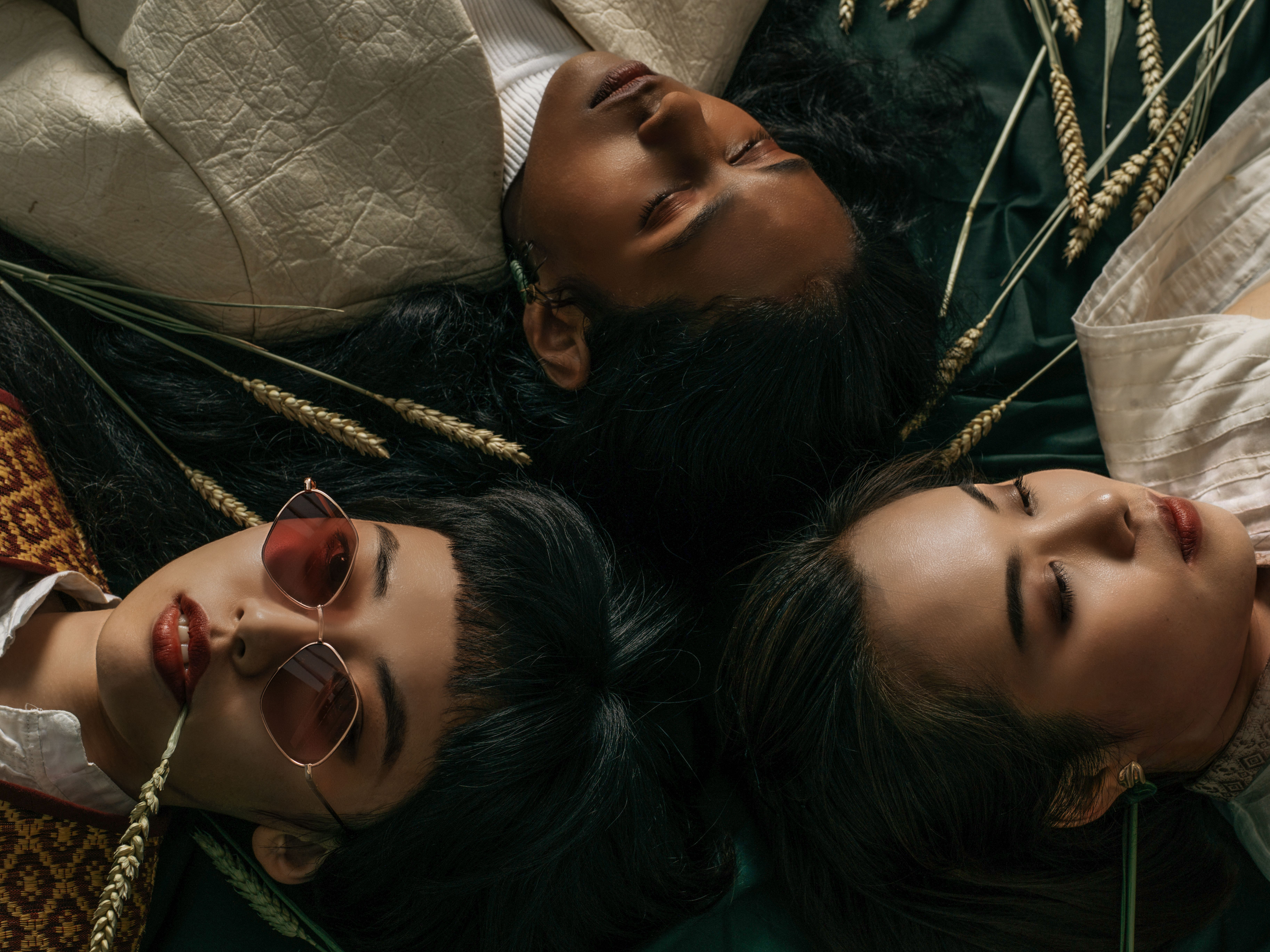 Close up overhead shot of 3 models relaxing, 2 with eyes closed amongst wheat grass