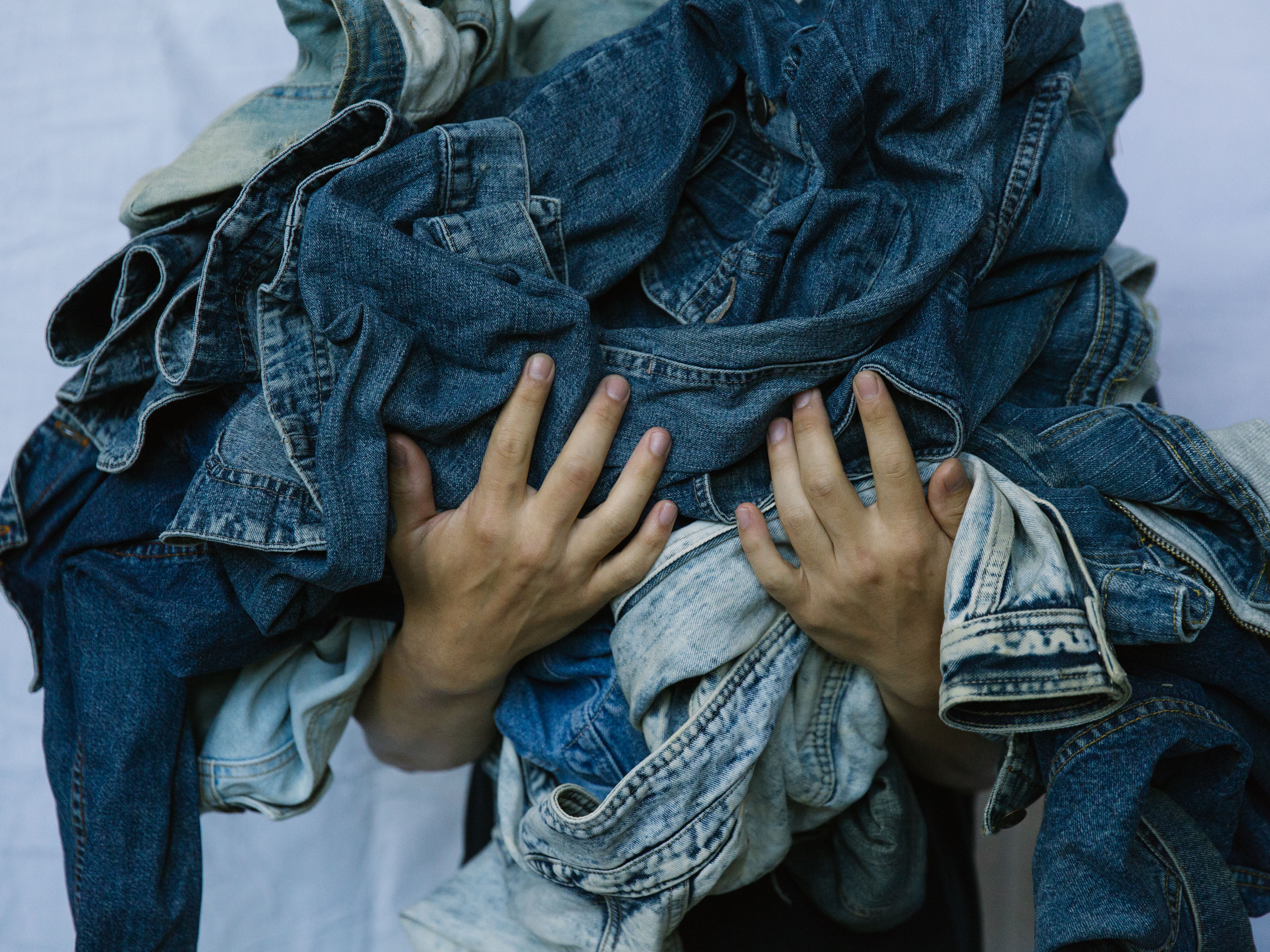 Two hands holding a pile of denim gsrments