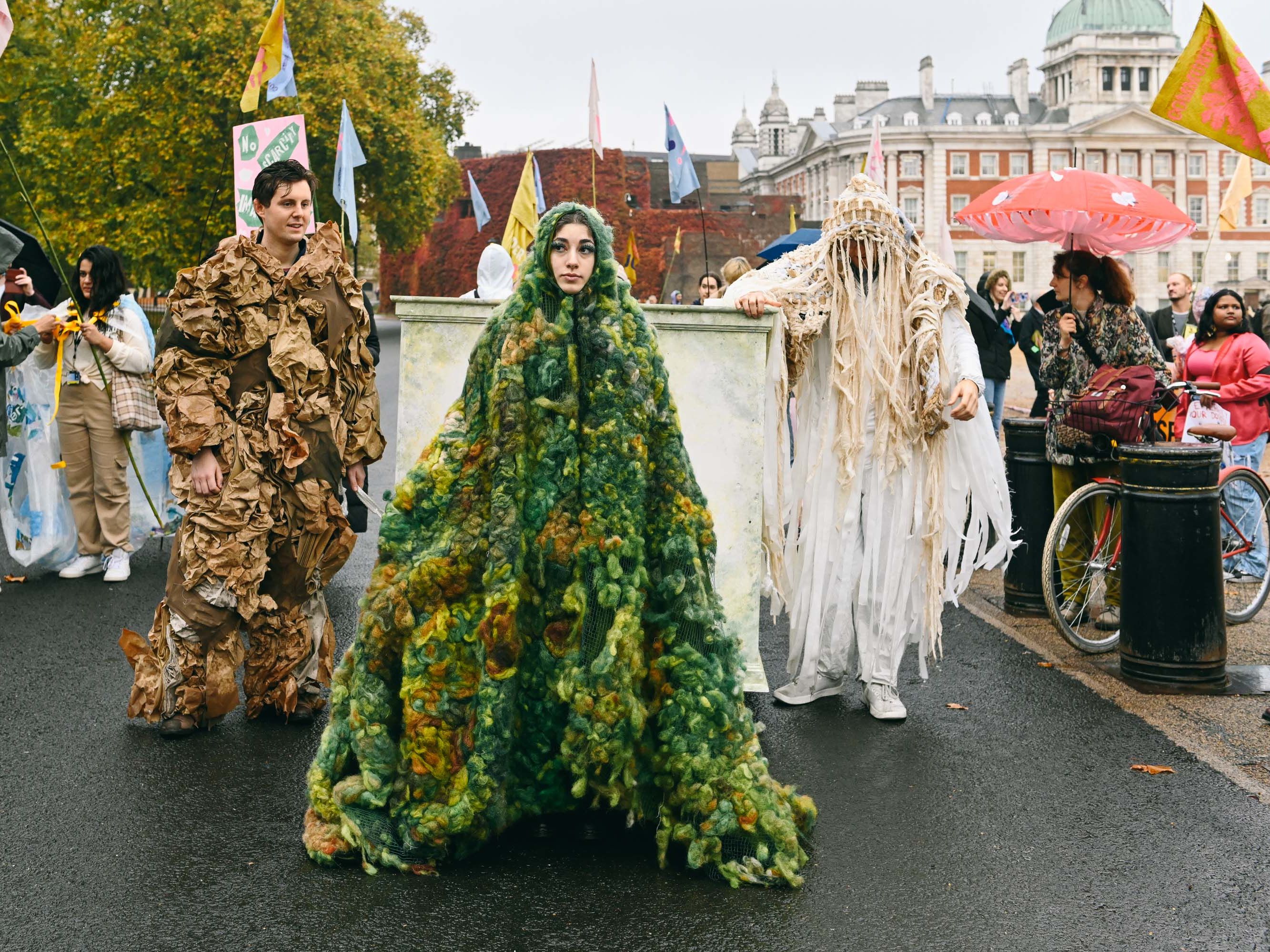 Figures standing  wearing green moss, cardboard and pale fabric garments