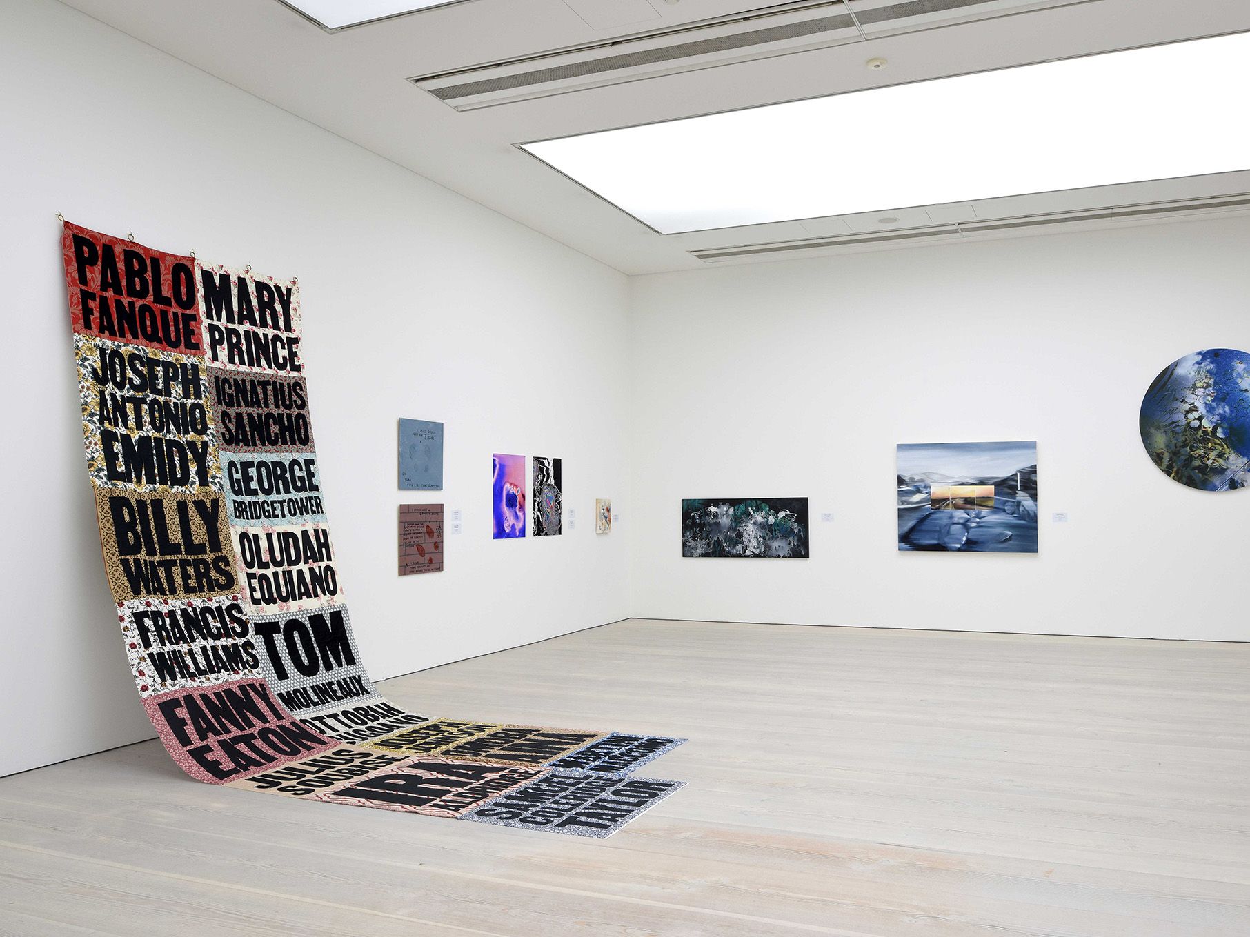 Installation view of several paintings and one large quilt hung on white wall