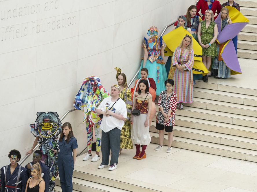 People in colourful costumes lined up on the interior steps of the British Museum, shot from below upwards