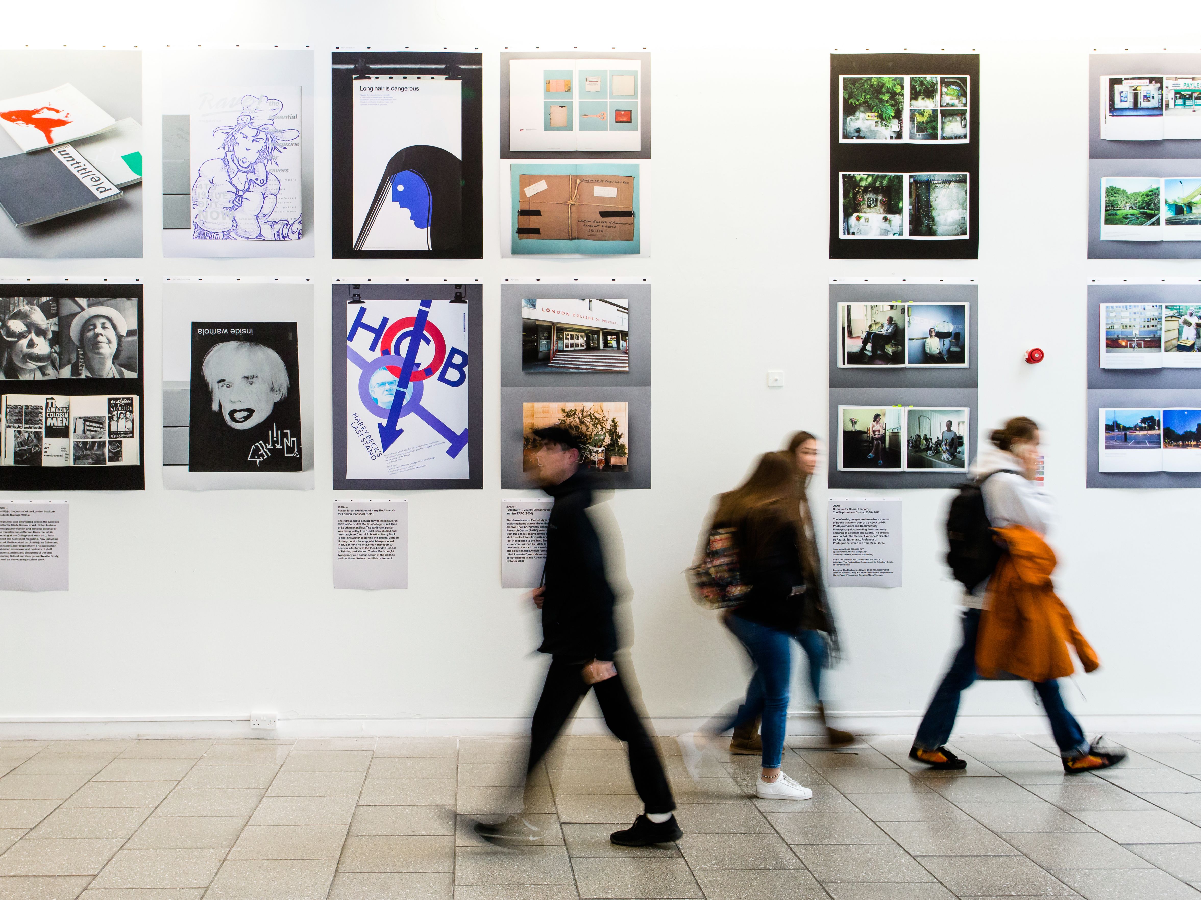 People walking past an exhibition wall, with their movement blurred.