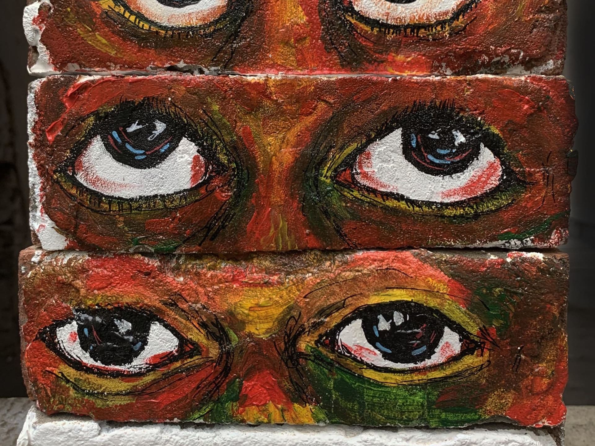 Large scale painting of 4 sets of eyes created using 4 horizontal rows of bricks stacked on top of each other, with intense colours 