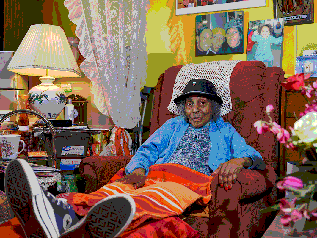 A woman sits in an armchair, surrounded by her living room.
