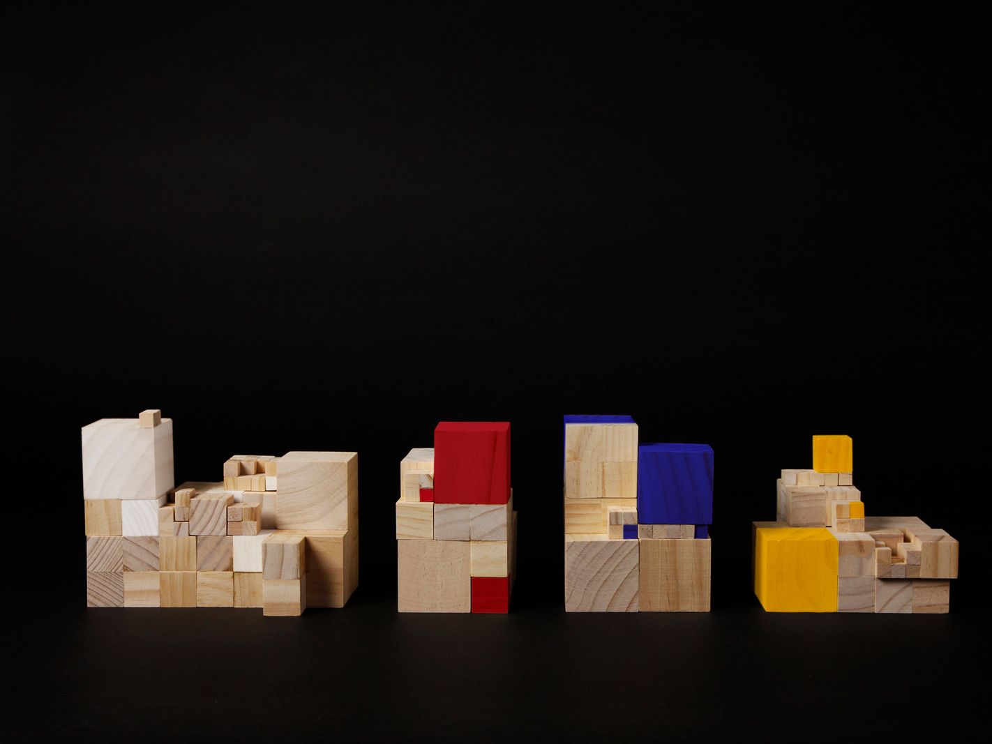 Wooden cube bricks, some coloured in red, yellow and blue, stacked into piles.