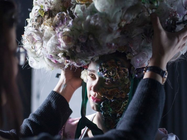 A model having a large floral headpiece adjusted on her head