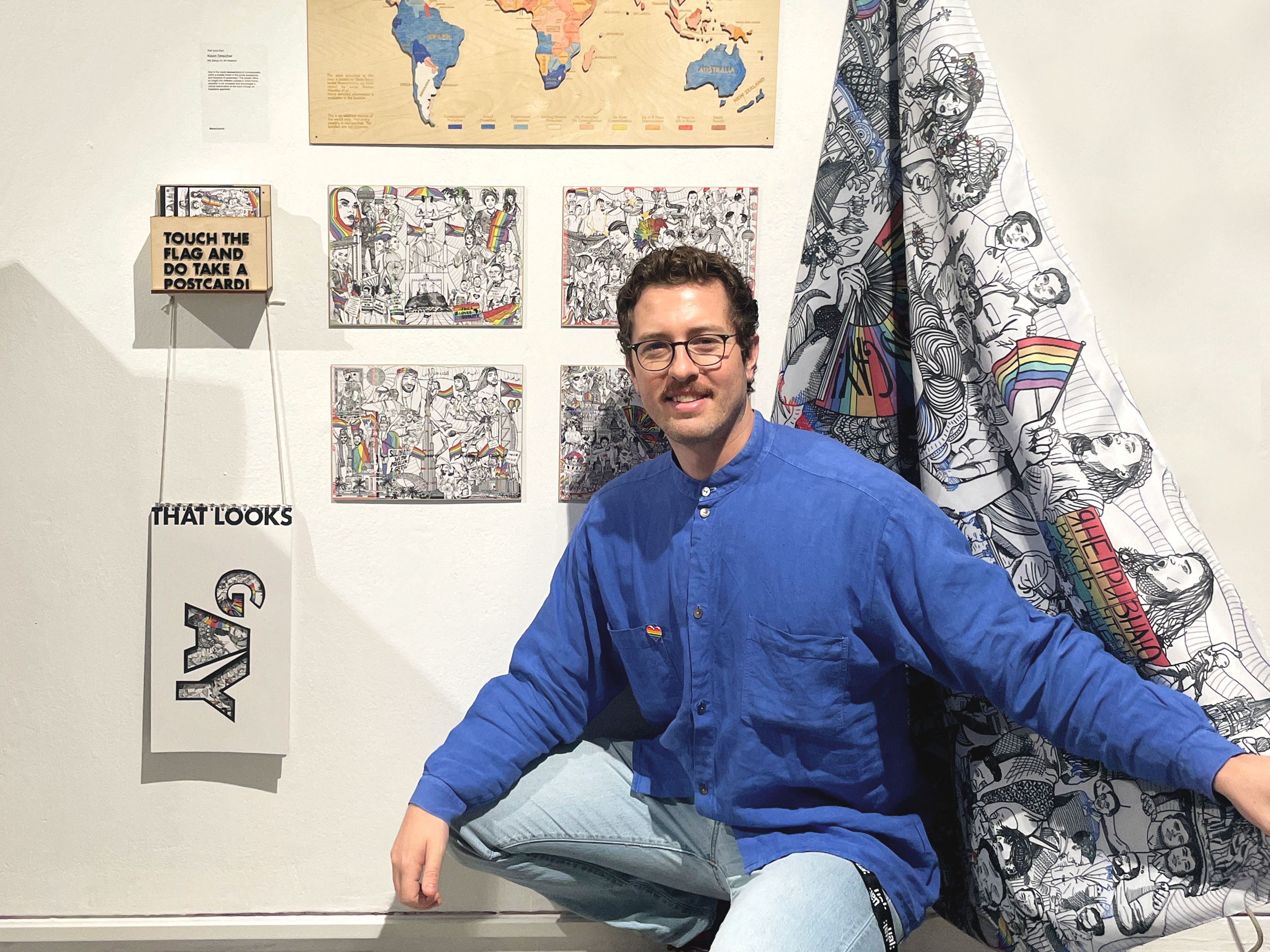 Student crouching down in front of their final project. The project consists of two large black and white illustrations and a flag