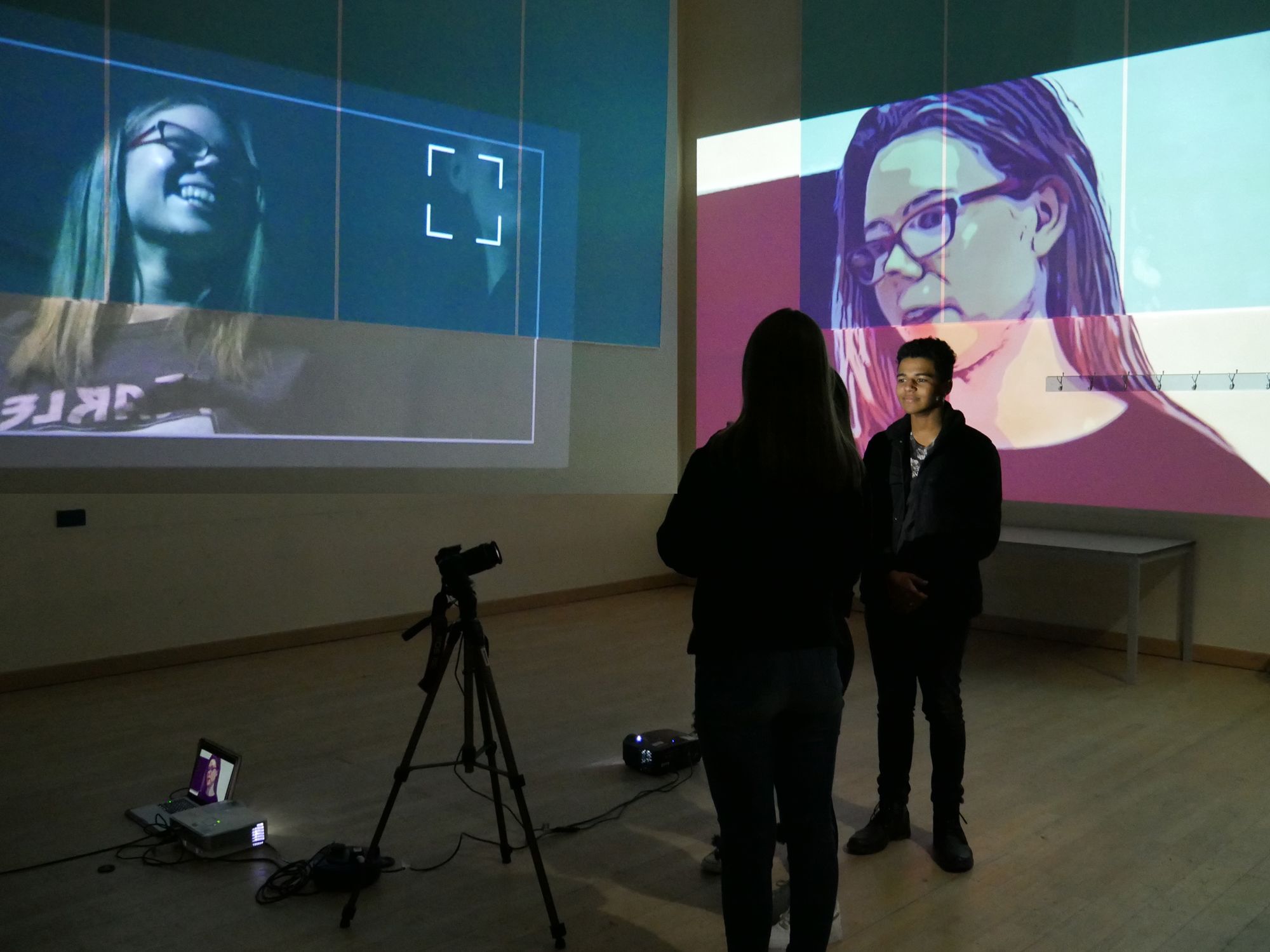 photograph of two students in a dark room with projections of their faces on walls