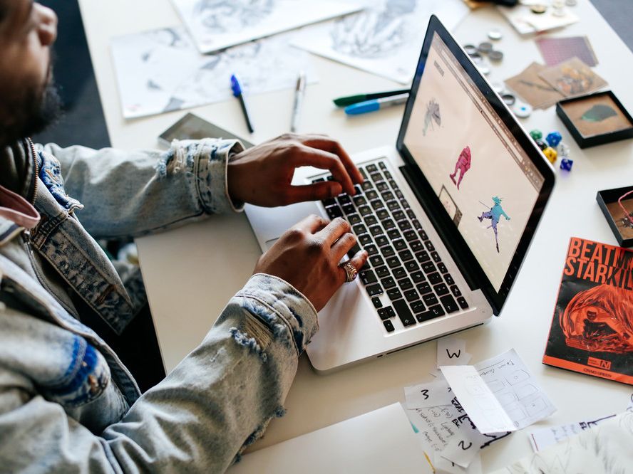 Student working on a laptop with sketches surrounding them.