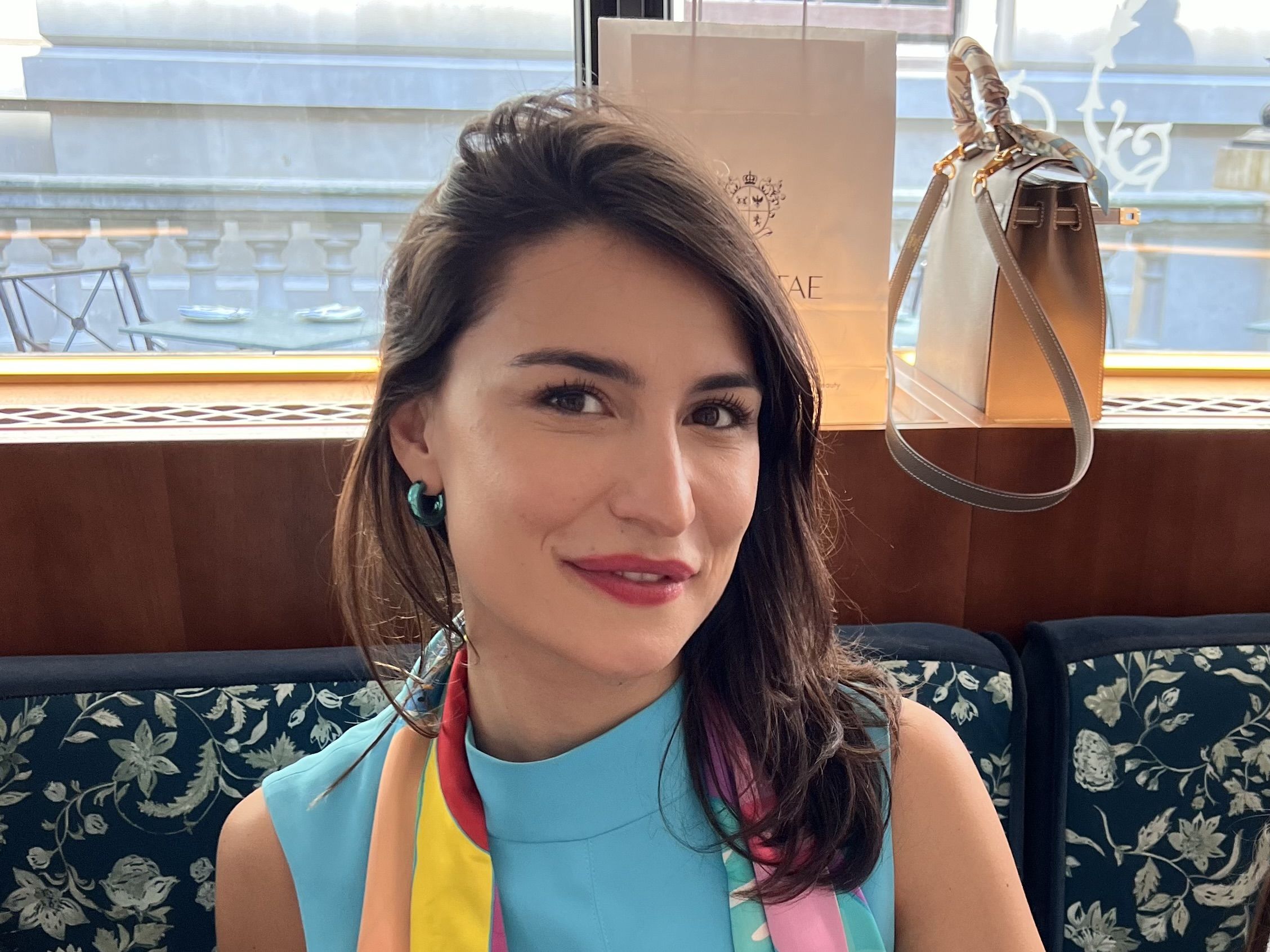 Tamta sitting looking directly into the camera. She's holding a small tan bag. 