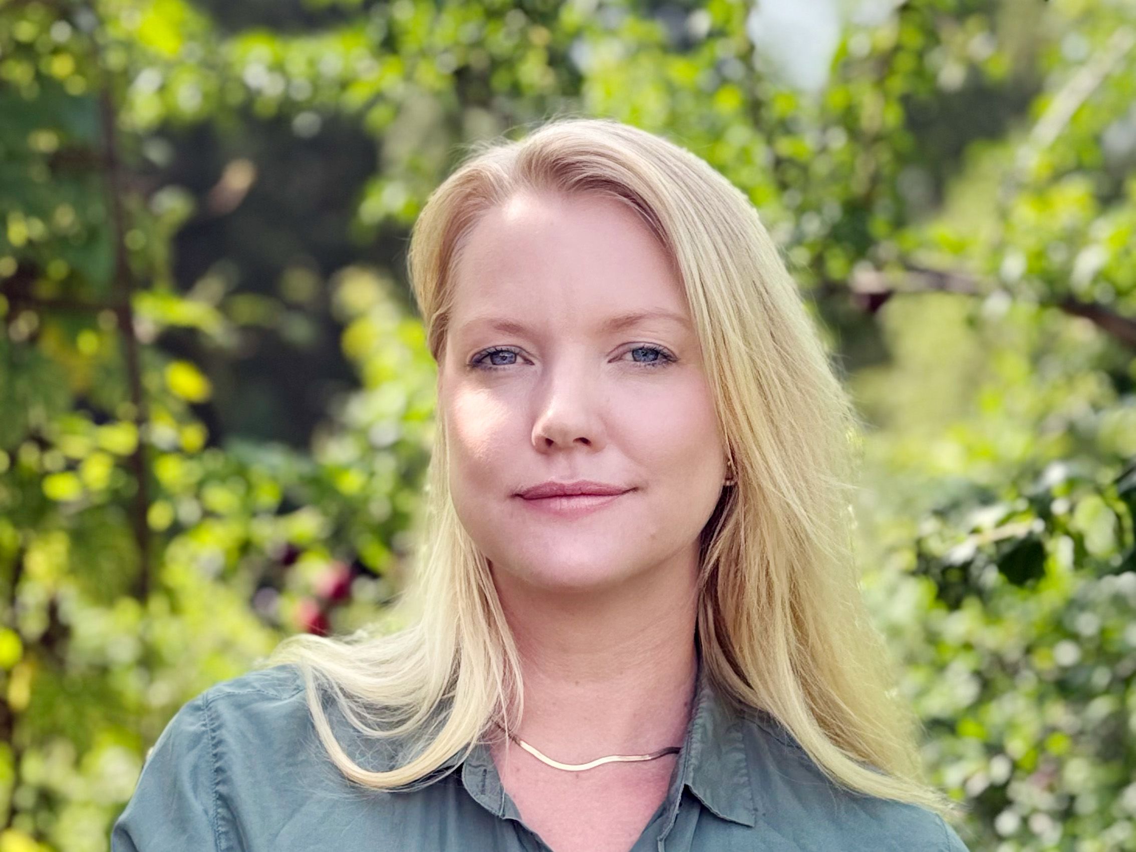 A blonde woman wearing a green blouse with leaves in the background
