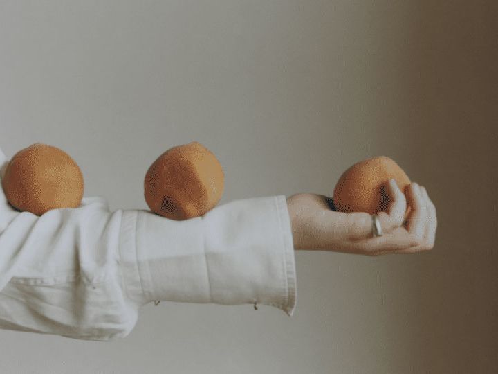 A girl balances three oranges on her arm.