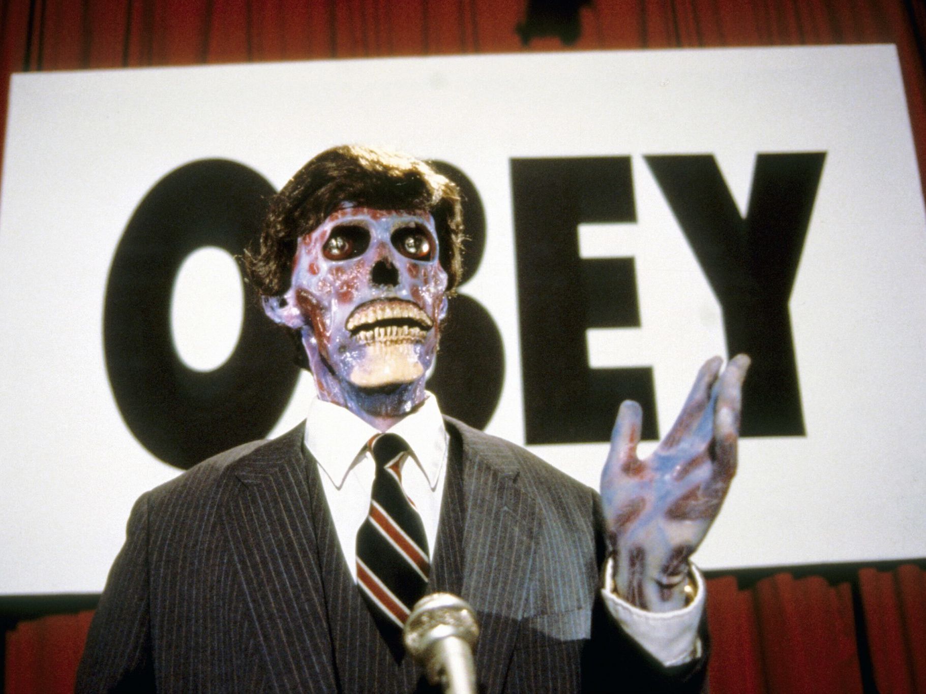 Skeleton in a suit next to sign that reads 'OBEY' 